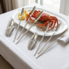 Set de utensilios para marisco con pinzas y tenedores junto a una langosta servida en plato blanco