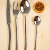 Imagen de cuberteria sobre fondo marron claro, chuchillo, tenedor, cucharagrande y pequeña. Pertenece al juego de cuberteria trento de 24 piezas de acero inoxidable.