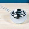 cazo de acero inoxidable napoles de 16 cm sobre un fondo de mesa de una cocina, se alcanza a visualizar parte de una cuchara de madera y un condimentero